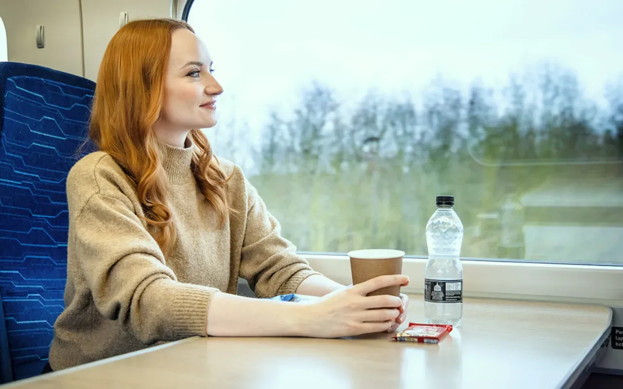 A passenger with drinks and a snack onboard a Hull Trains service looking out the window